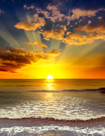 Majestic bright sunrise over the ocean. Calm sea and orange clouds.